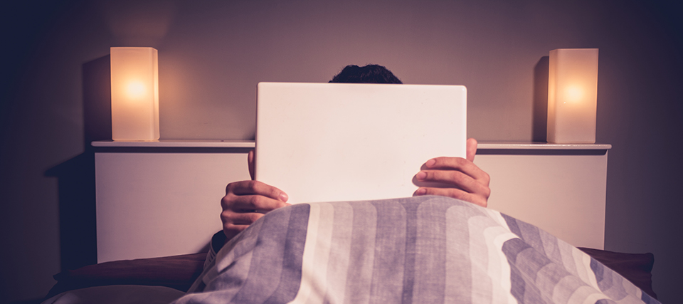 Man is sitting in bed behind his laptop likely watching porn