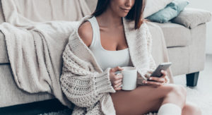 Woman lounges beside her couch with coffee and her phone - sexting her lover